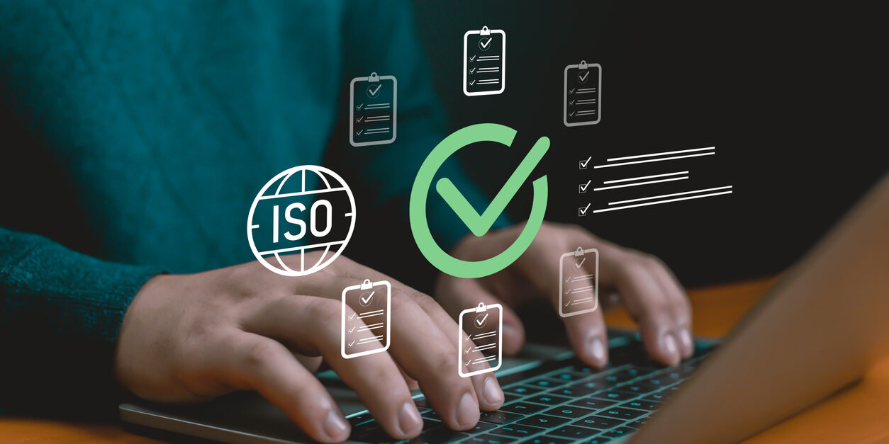 Hands typing on laptop with ISO certification icons, checklist, and approval mark, symbolizing quality assurance, compliance, audit process, business standards, certification, and corporate solutions.