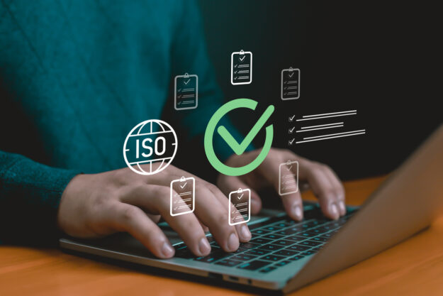 Hands typing on laptop with ISO certification icons, checklist, and approval mark, symbolizing quality assurance, compliance, audit process, business standards, certification, and corporate solutions.